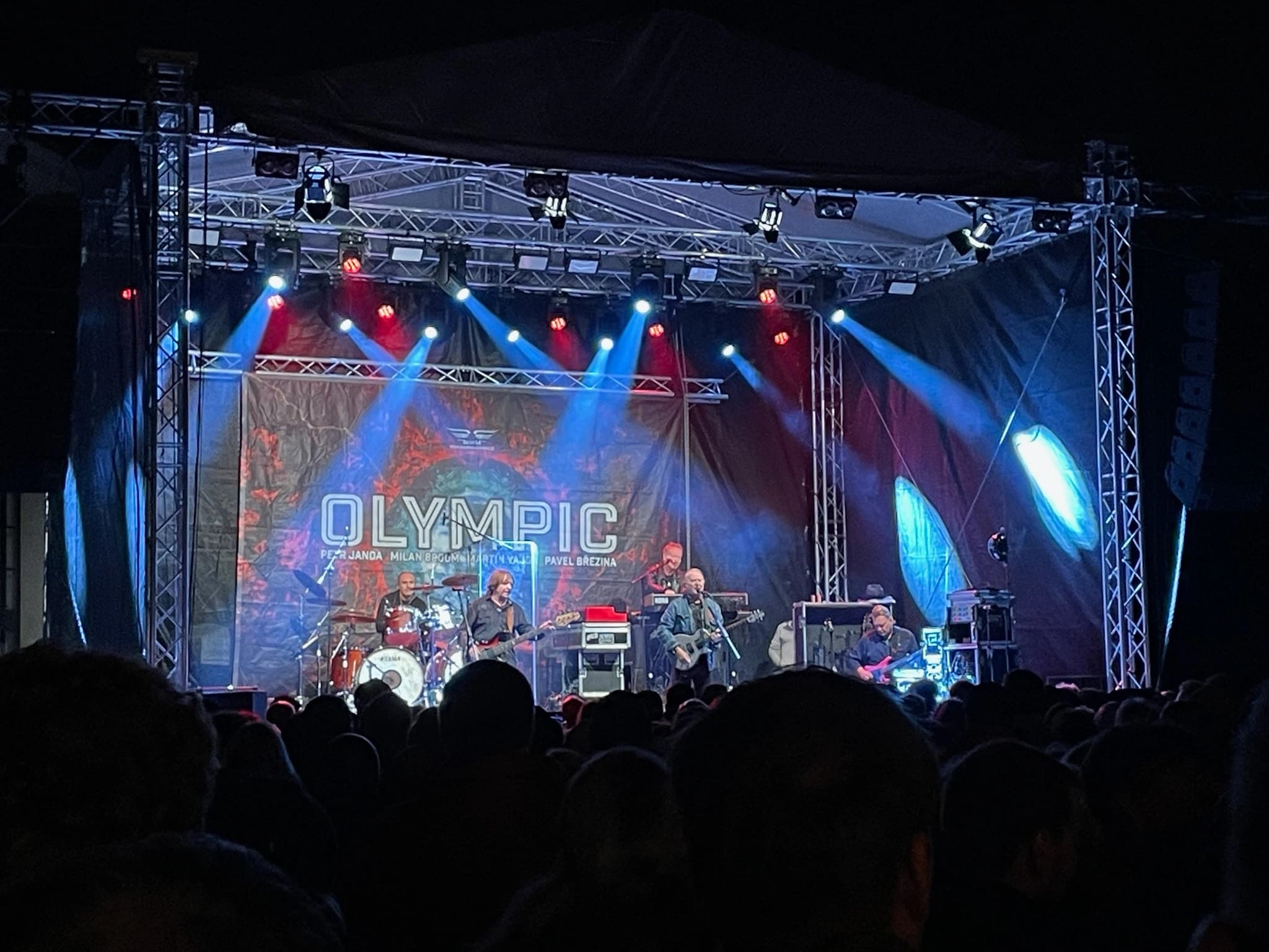 Koncert kapely Olympic na venkovním pódiu s modrými světly
