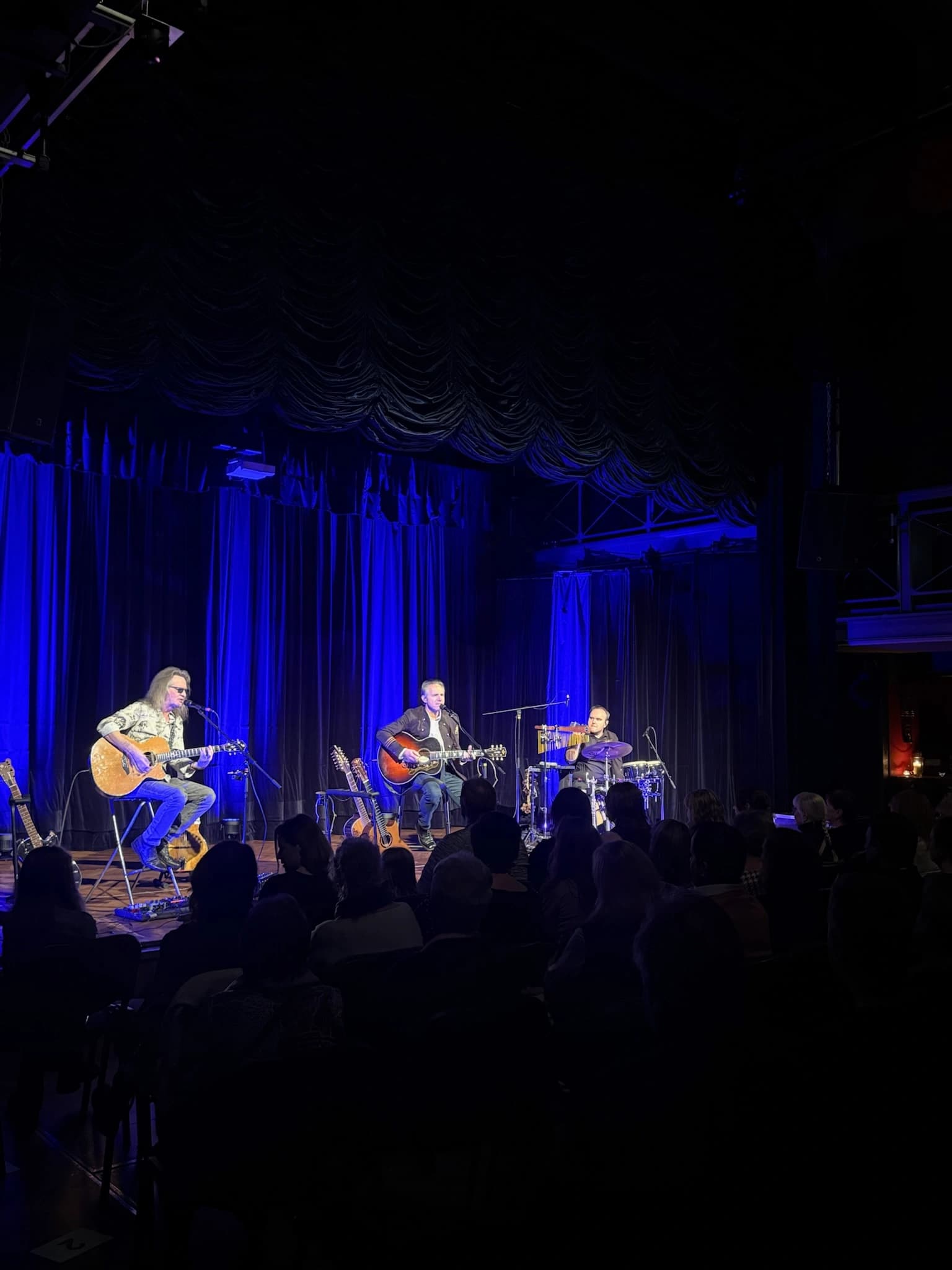 Akustické hudební trio na pódiu s modrým scénickým osvětlením